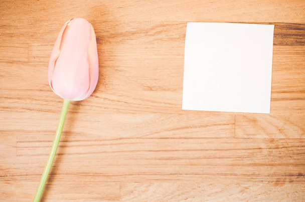 An overhead shot of a pink tulip flower and a blank sticky note on a wooden table with space for your text - Foto, Imagen