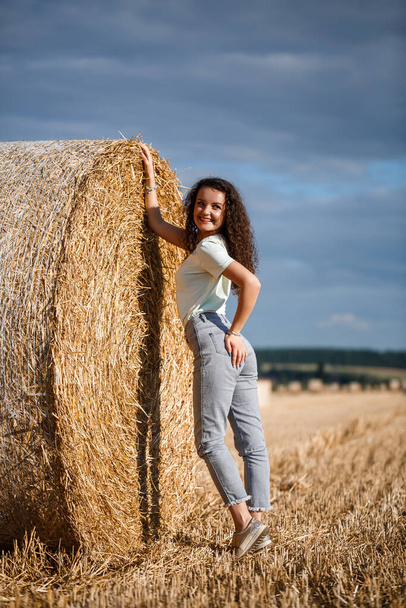 Красивая девушка возле тюков сена в сельской местности. Девушка на фоне стога сена - Фото, изображение