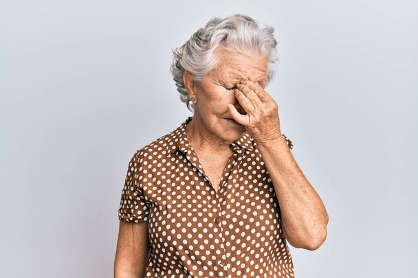 Starší šedovlasá žena v neformálním oblečení, unavená třením nosu a očí, pociťující únavu a bolest hlavy. koncepce stresu a frustrace.  - Fotografie, Obrázek