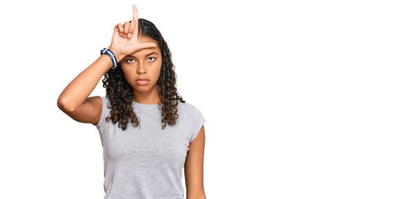 Nuori afrikkalainen amerikkalainen tyttö yllään rento vaatteita pilkata ihmisiä, joilla on sormet otsa tekee luuseri ele pilkkaa ja loukkaavaa.  - Valokuva, kuva