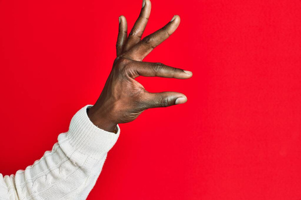 Arm and hand of african american black young man over red isolated background picking and taking invisible thing, holding object with fingers showing space  - Фото, зображення