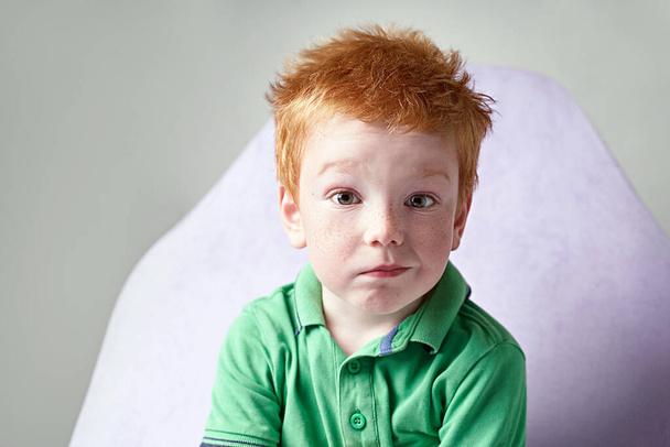 Cute red haired freckled little boy in green t-shirt waiting for doctor in medical office - Фото, изображение