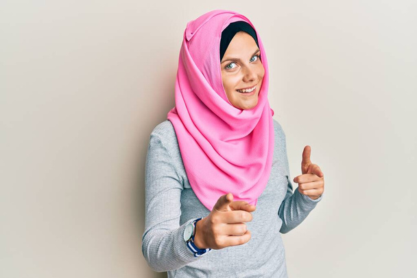 Young caucasian woman wearing traditional islamic hijab scarf pointing fingers to camera with happy and funny face. good energy and vibes.  - Fotoğraf, Görsel