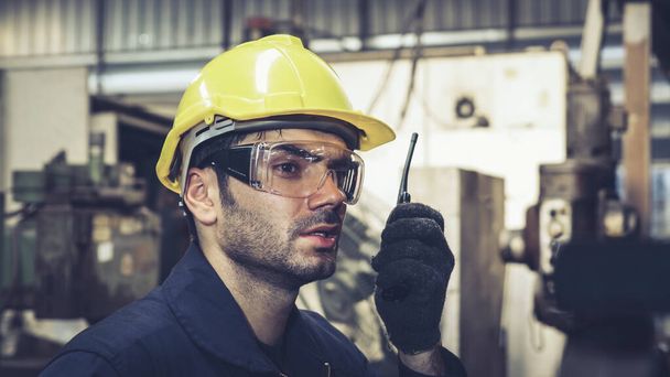 Trabajador de fábrica hablando por radio portátil mientras inspecciona piezas de maquinaria - Foto, Imagen