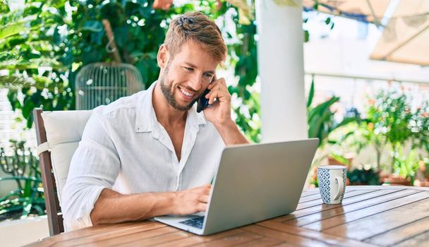 Jóképű kaukázusi férfi ül a teraszon dolgozik otthonról számítógép laptop és telefonon beszél - Fotó, kép