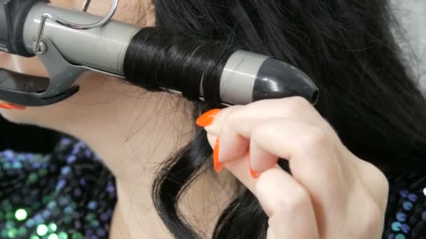 Eine schöne, spektakuläre junge Frau wickelt ihre langen schwarzen Haare auf einem speziellen Bügeleisen, um Locken aus nächster Nähe zu schaffen - Filmmaterial, Video
