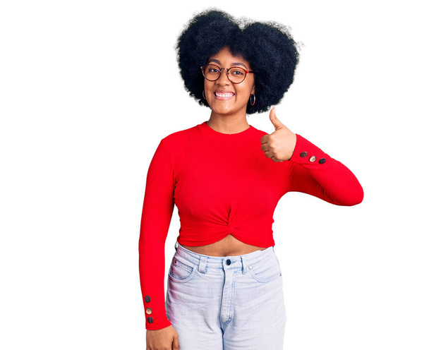 Młoda Afroamerykanka w luźnych ciuchach i okularach, wykonująca gesty ręką w górę. zatwierdzanie ekspresji patrząc w aparat pokazujący sukces.  - Zdjęcie, obraz