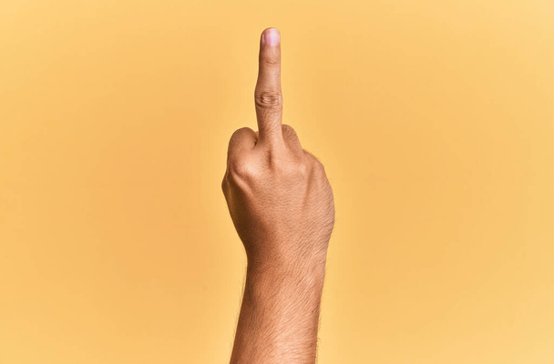 Arm and hand of caucasian man over yellow isolated background showing provocative and rude gesture doing fuck you symbol with middle finger  - Foto, afbeelding