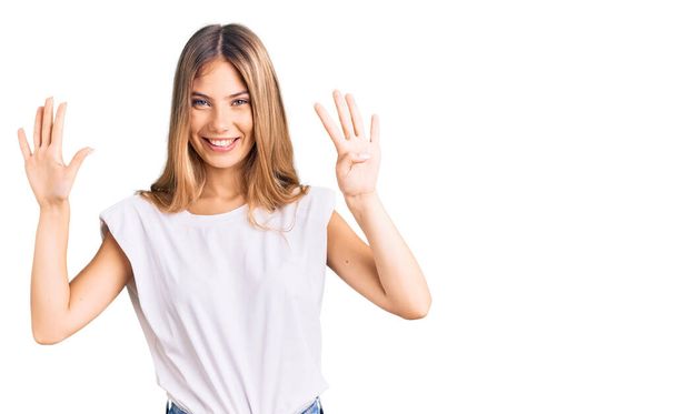 Beautiful caucasian woman with blonde hair wearing casual white tshirt showing and pointing up with fingers number nine while smiling confident and happy.  - Фото, изображение