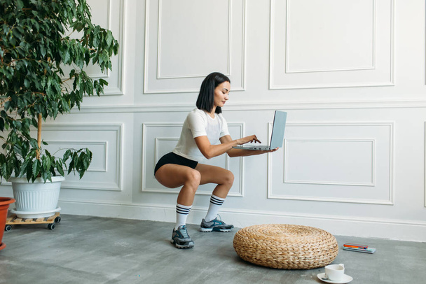 young beautiful girl with Asian appearance, fitness instructor, she conducts a web conference on fitness classes, she has a laptop and a phone in her hands - Φωτογραφία, εικόνα
