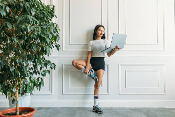 young beautiful girl with Asian appearance, fitness instructor, she conducts a web conference on fitness classes, she has a laptop and a phone in her hands - Photo, image