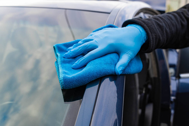 Hände in blauen Gummihandschuhen reiben das Auto mit einem blauen Mikrofasertuch ein. Polieren und Waschen von Autos. Nahaufnahme - Foto, Bild