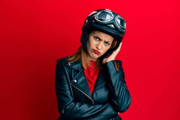 Ισπανόφωνη νεαρή γυναίκα φορώντας κράνος μοτοσικλέτας σκέφτεται κουρασμένος και βαρεθεί με προβλήματα κατάθλιψης με σταυρωμένα χέρια.  - Φωτογραφία, εικόνα