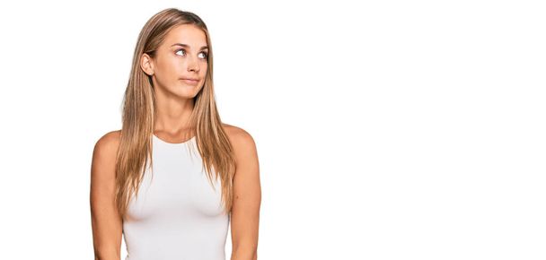 Young blonde woman wearing casual style with sleeveless shirt smiling looking to the side and staring away thinking.  - Photo, image