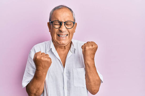 Handsome mature senior man wearing casual shirt and glasses celebrating surprised and amazed for success with arms raised and eyes closed  - Photo, Image
