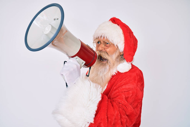 Old senior man wearing santa claus traditional costume shouting through megaphone - Foto, afbeelding