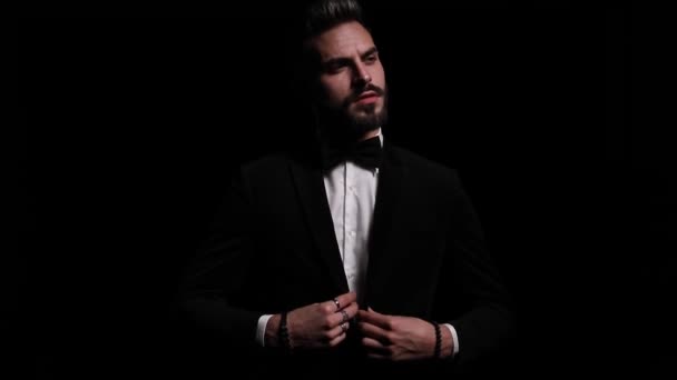 sexy jonge zakenman knopen zwarte smoking, kruising armen, op zoek naar kant en poseren, knipogen en lachen op zwarte achtergrond in de studio - Video