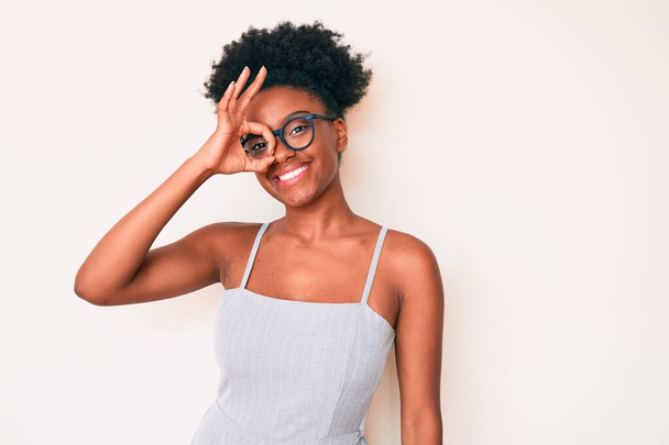 Молода афроамериканка, одягнена в повсякденний одяг і окуляри посміхається, що радісно робить знак з рукою на очі дивлячись через пальці  - Фото, зображення