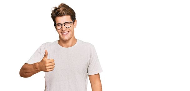 Handsome caucasian man wearing casual clothes and glasses doing happy thumbs up gesture with hand. approving expression looking at the camera showing success.  - Photo, Image