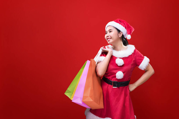 A beautiful woman in Santa Claus costume holding shopping bags on occasion of the Merry Christmas and Happy New Year. - Zdjęcie, obraz