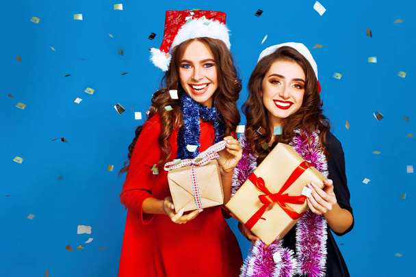 Świąteczne młode kobiety. Uśmiechnięte kobiety w kapeluszu Świętego Mikołaja trzymające wiele pudełek z prezentami. Urlop zimowy. - Zdjęcie, obraz