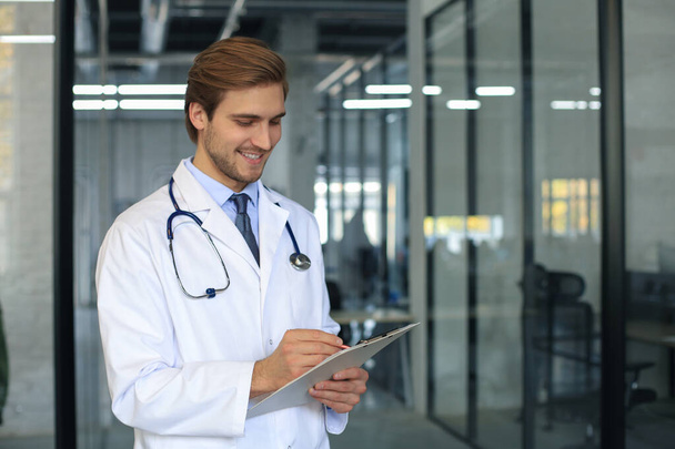 Portrait of doctor standing in hospital corridor wearing lab coat and stethoscope - 写真・画像
