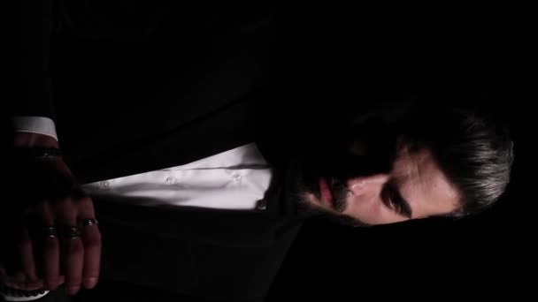 sexy elegantní muž dotýkající se prstů, dívající se na stranu a přemýšlející, aranžující černý smoking, smyslně chytající krk a pózující v módním světle na tmavém pozadí ve studiu - Záběry, video