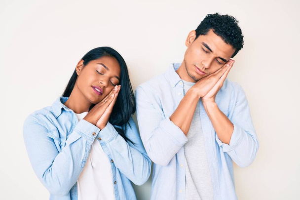 Красивая латинская молодая пара в повседневной одежде спит усталый сон и позирует с руками вместе, улыбаясь с закрытыми глазами.  - Фото, изображение