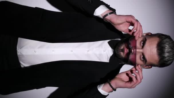сексуальна молода модель кнопка чорного оксамитового тукседо, одягаючи сонцезахисні окуляри, перетинаючи руки, ламаючи пальці і вмикаючи сірий фон в студії
 - Кадри, відео