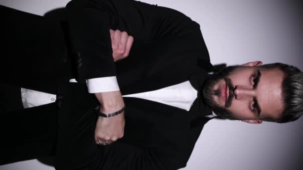 verticaal portret van elegante jonge man vouwen armen, aanpassen strikje, knop zwart fluweel smoking en op zoek naar kant op grijze achtergrond in de studio - Video