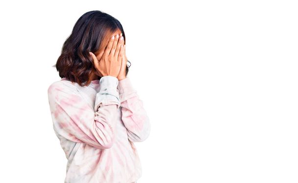 泣きながら手で顔を覆う悲しい表情でカジュアルなネクタイ染めのスウェットシャツを着た若い美しい混合レースの女性。うつ病の概念.  - 写真・画像