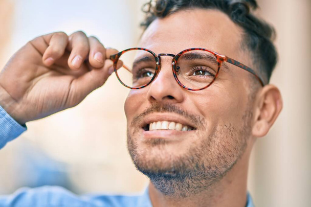 Giovane uomo d'affari ispanico sorridente felice toccando i suoi occhiali in città. - Foto, immagini