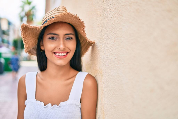 Joven chica latina con estilo veraniego y sonriente feliz apoyada en la pared. - Foto, imagen
