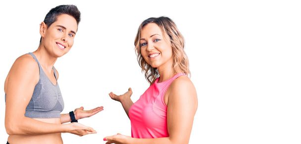 Couple de femmes portant des vêtements de sport invitant à entrer souriant naturel avec la main ouverte  - Photo, image