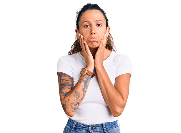 Young hispanic woman with tattoo wearing casual white tshirt tired hands covering face, depression and sadness, upset and irritated for problem  - Фото, изображение