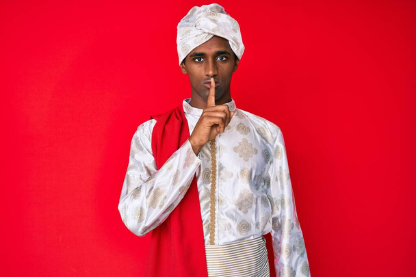 Schöner indischer Mann in traditioneller Sherwani-Sararee-Kleidung, der darum bittet, mit dem Finger auf den Lippen ruhig zu sein. Schweigen und geheimes Konzept.  - Foto, Bild