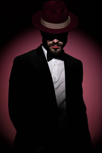 homme d'affaires mystérieux sexy couvert d'ombres porte un chapeau bordeaux et posant avec attitude - Photo, image