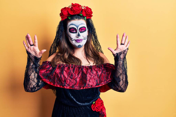 Young woman wearing day of the dead costume over yellow showing and pointing up with fingers number ten while smiling confident and happy.  - Photo, Image