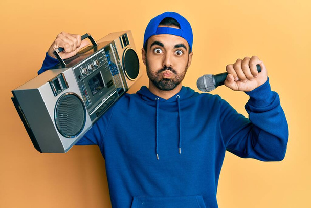 Young hispanic man with beard holding boombox listening to music singing with microphone skeptic and nervous, frowning upset because of problem. negative person.  - Photo, Image