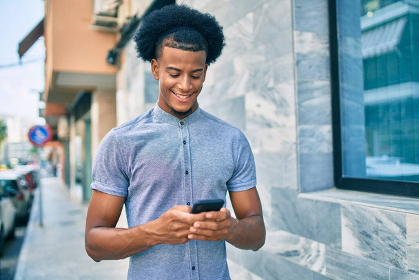 Nuori afrikkalainen amerikkalainen mies hymyilee onnellisena älypuhelimella kaupungissa. - Valokuva, kuva