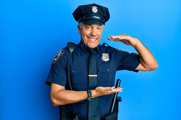 Красивый зрелый мужчина средних лет в полицейской форме жестикулирует руками, показывая большой и большой знак, символ меры. улыбаясь, глядя в камеру. концепция измерения.  - Фото, изображение