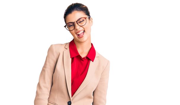 Νεαρή όμορφη γυναίκα με επιχειρηματικό πουκάμισο και γυαλιά να κλείνει το μάτι κοιτάζοντας την κάμερα με σέξι έκφραση, χαρούμενο και χαρούμενο πρόσωπο.  - Φωτογραφία, εικόνα