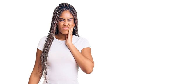 Junge afrikanisch-amerikanische Frau mit Zöpfen in lässiger Kleidung berührt Mund mit Hand mit schmerzhaftem Gesichtsausdruck wegen Zahnschmerzen oder Zahnerkrankungen an den Zähnen. Zahnarzt  - Foto, Bild