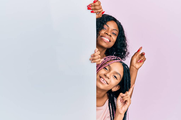 美しいアフリカ系アメリカ人の母親と娘を保持しています空のバナー笑顔幸せなポインティングとともに手と指で側面  - 写真・画像