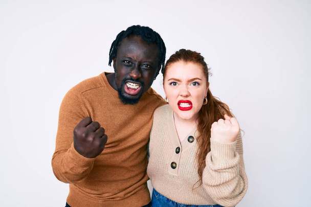 Interracial couple wearing casual clothes angry and mad raising fist frustrated and furious while shouting with anger. rage and aggressive concept.  - Foto, immagini