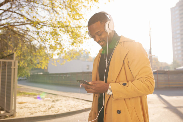 African American man listening to music with headphones on head walking in city - Photo, Image