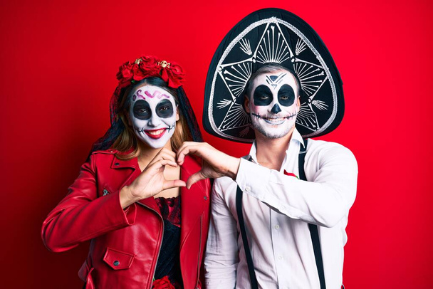 Couple wearing day of the dead costume over red smiling in love showing heart symbol and shape with hands. romantic concept.  - Φωτογραφία, εικόνα