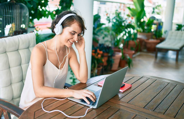 若い美しい白人女性は家から仕事をして幸せな笑顔とヘッドフォンを着て音楽を聴く - 写真・画像