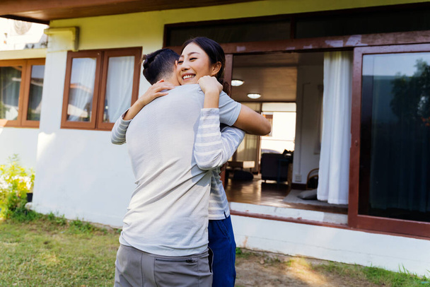 Portrait of young adult Asian couple embracing together with home interior in background. 30s happy mature husband and wife smiling and hugging each other in front of their house - with copy space. - 写真・画像