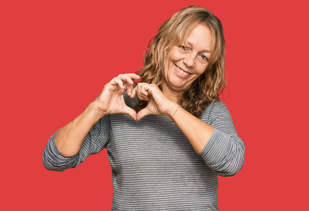 Middle age blonde woman wearing casual clothes smiling in love showing heart symbol and shape with hands. romantic concept.  - Photo, Image
